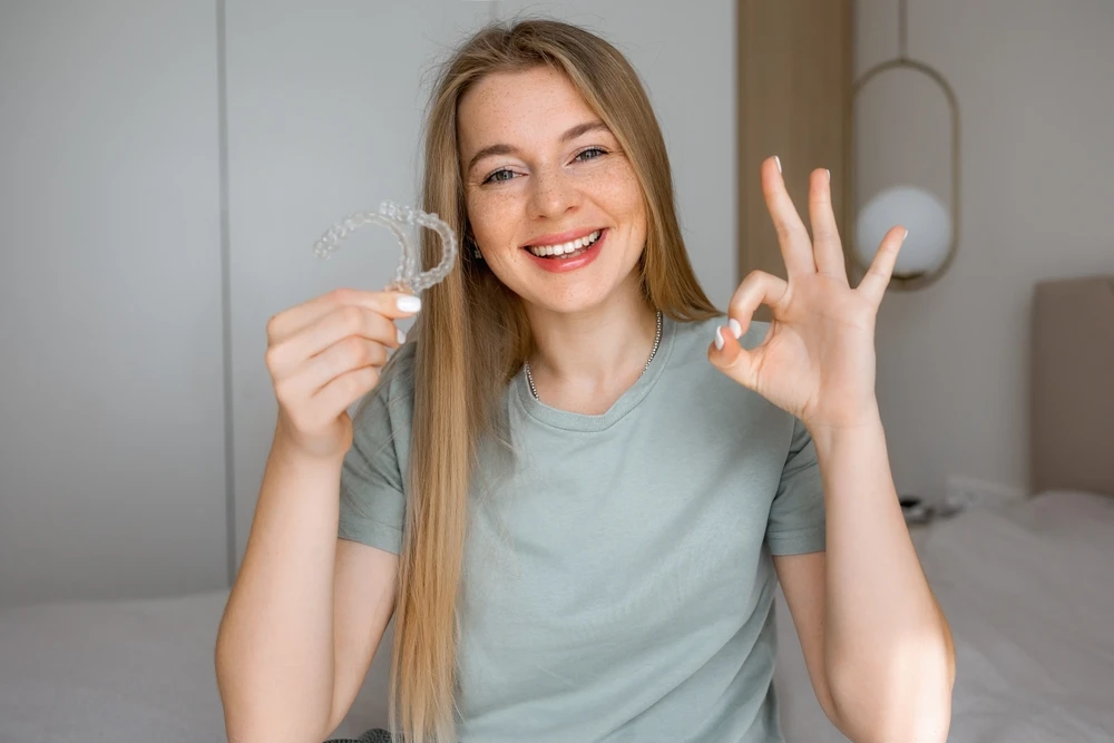 Smiling woman holding a clear dental aligner