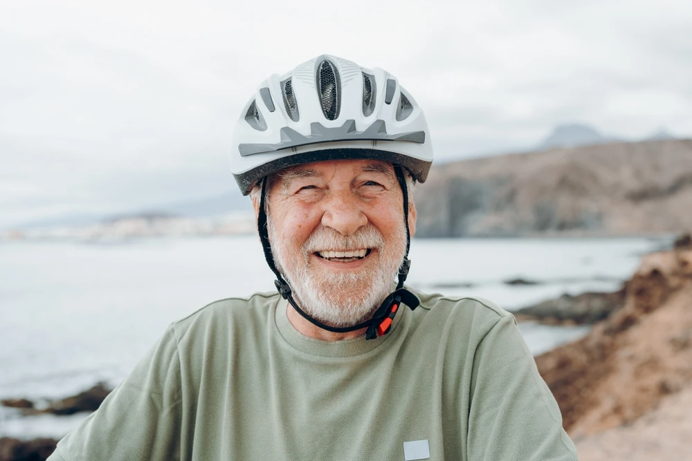 Smiling older man wearing a bicycle helmet beside the coast