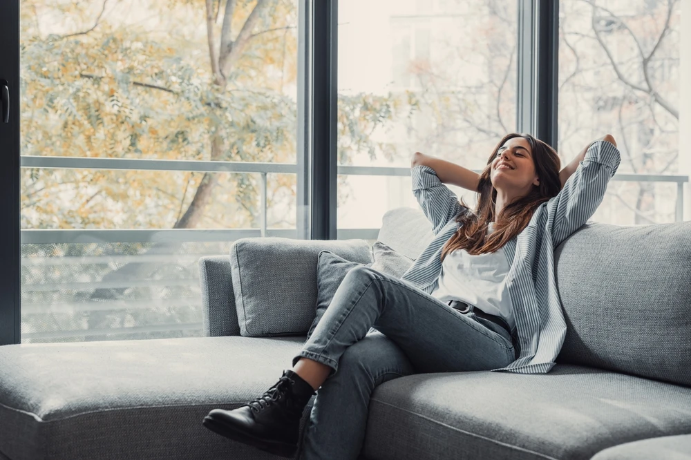 Woman relaxing on a sofa beside large windows